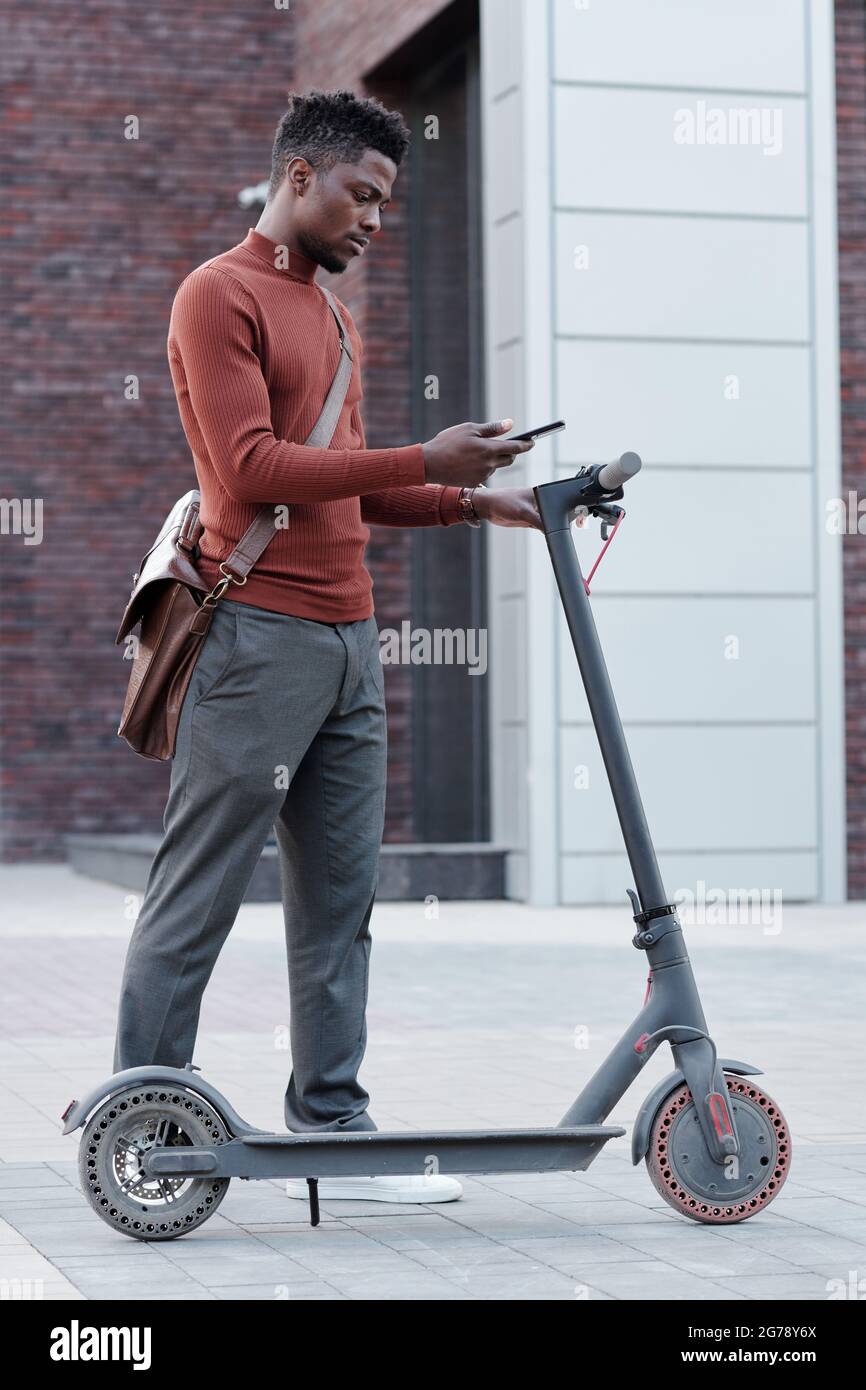 African guy with smartphone going to rent scooter to go to work Stock Photo