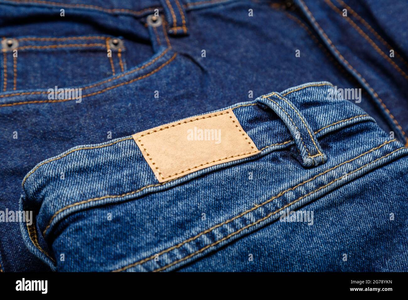 Blue denim jeans with emty label. Brown blank leather label tag on denim pants background. Blank mockup beige leather label. Close up Stock Photo