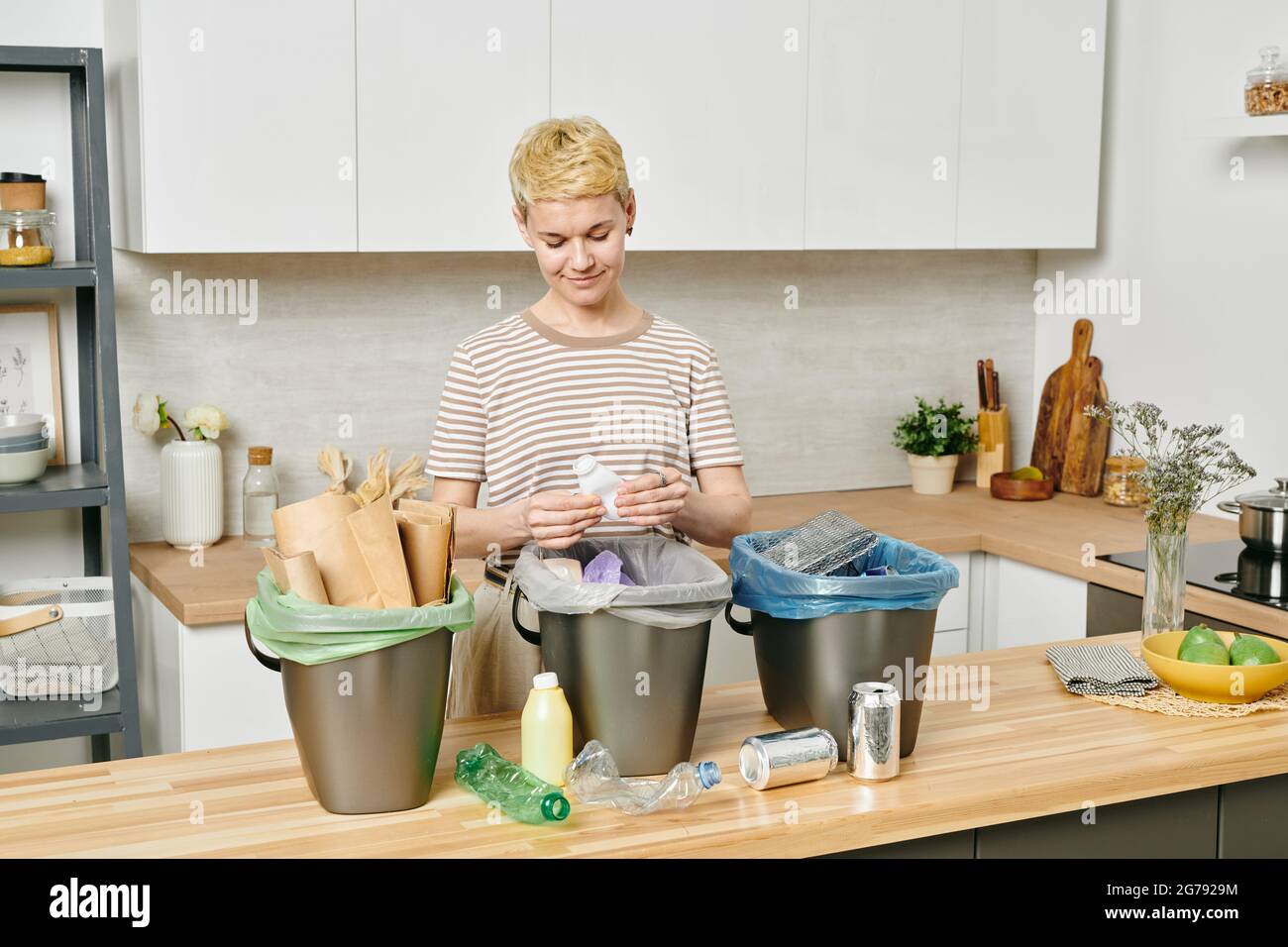 Pretty female sorting various kinds of trash into three bins Stock Photo