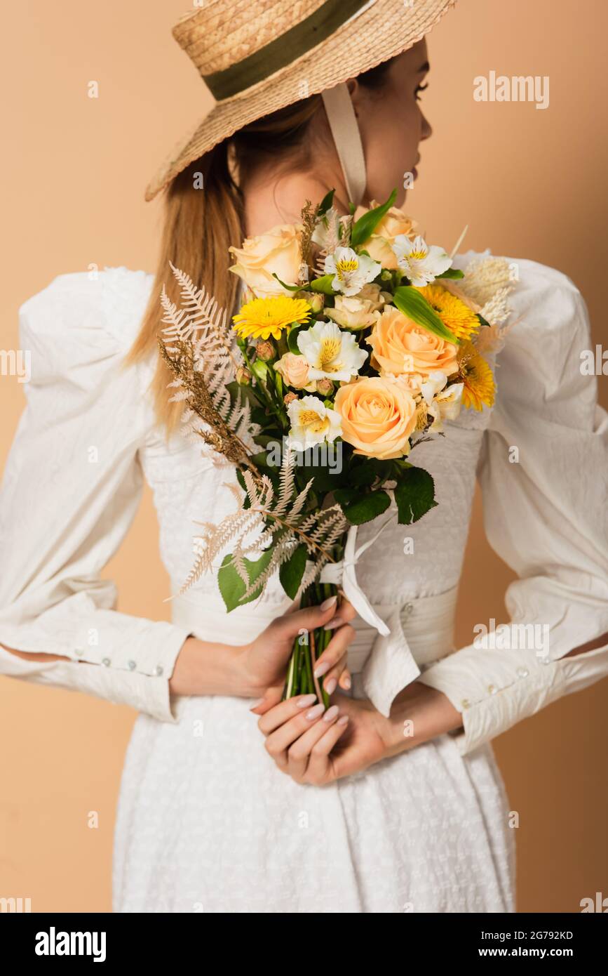 young woman in straw hat holding bouquet of flowers behind back on ...