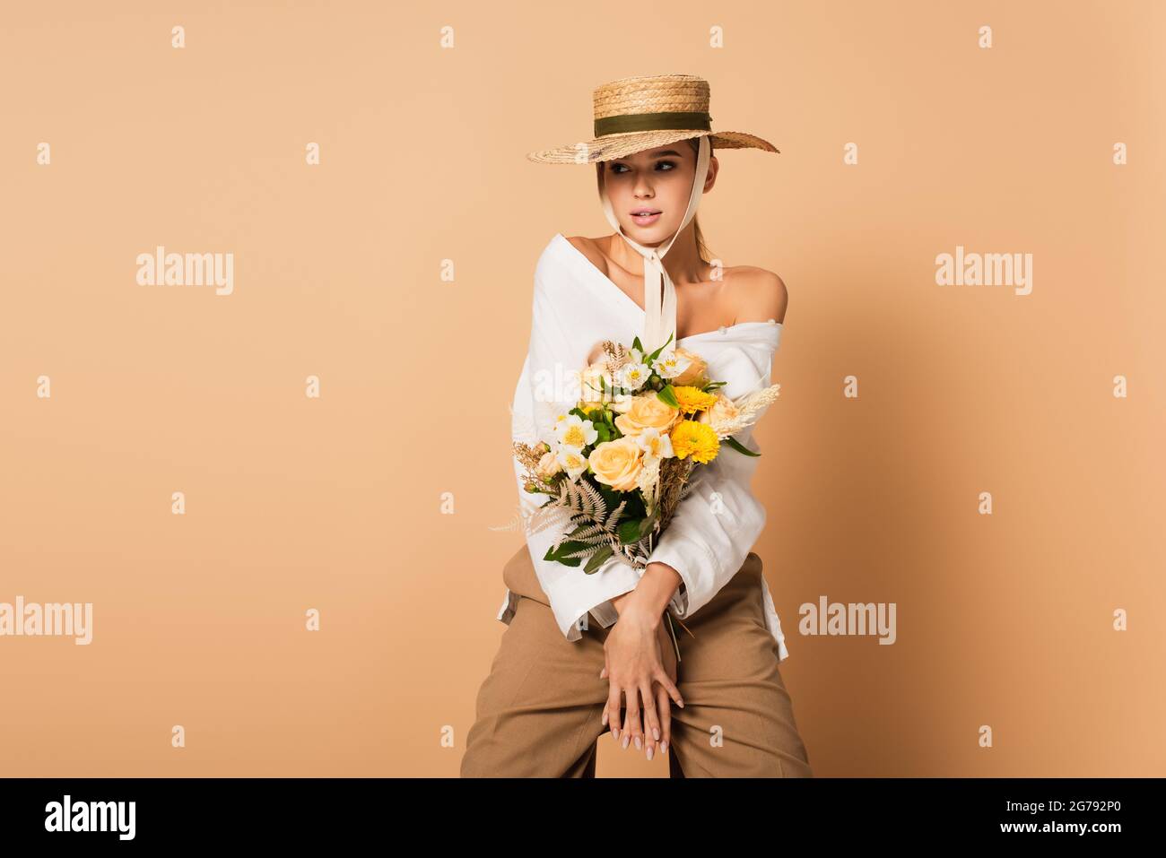 young woman in straw hat holding bouquet of flowers on beige Stock ...