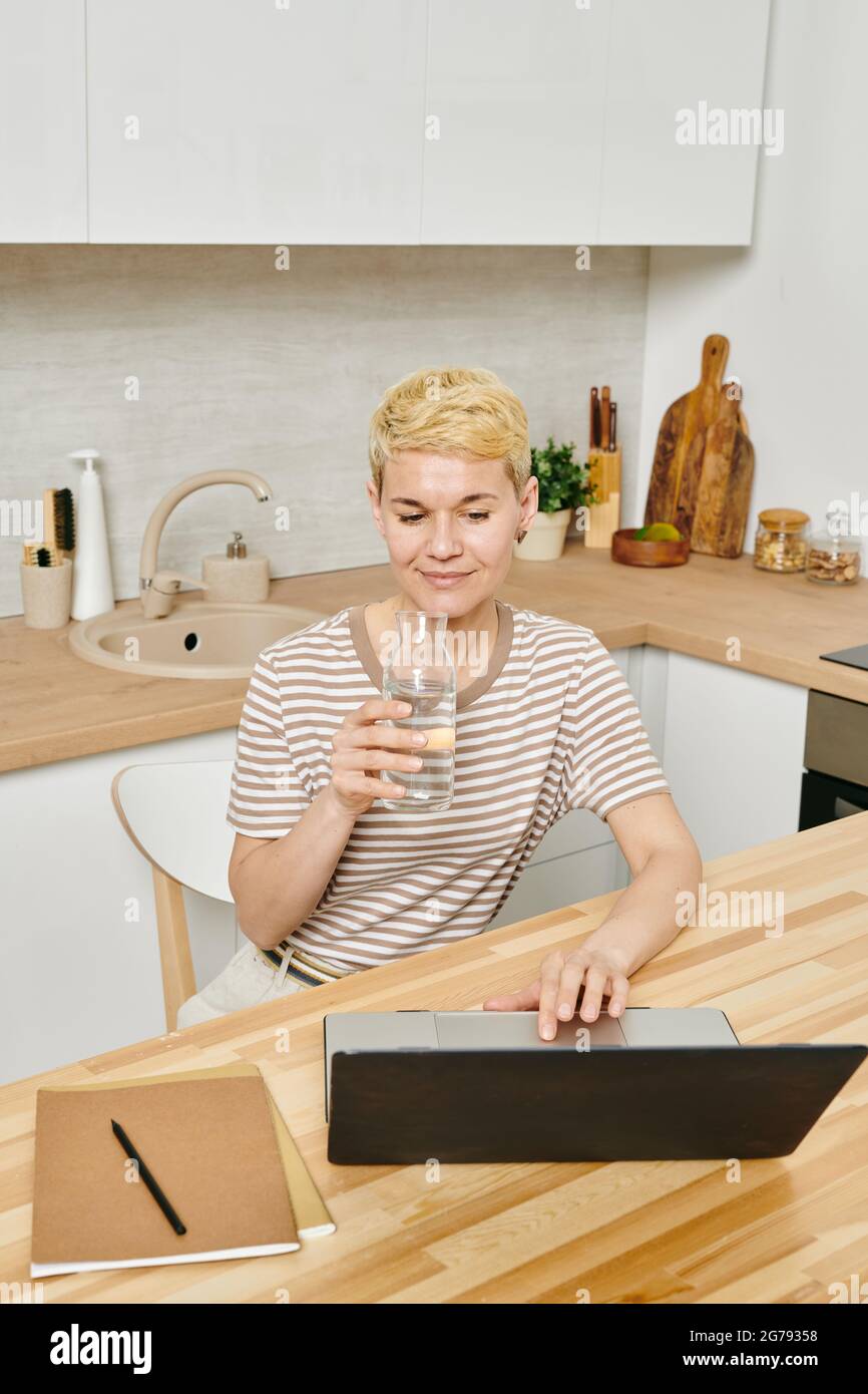 Businesswoman with glass of pure water using laptop in the kitchen Stock Photo