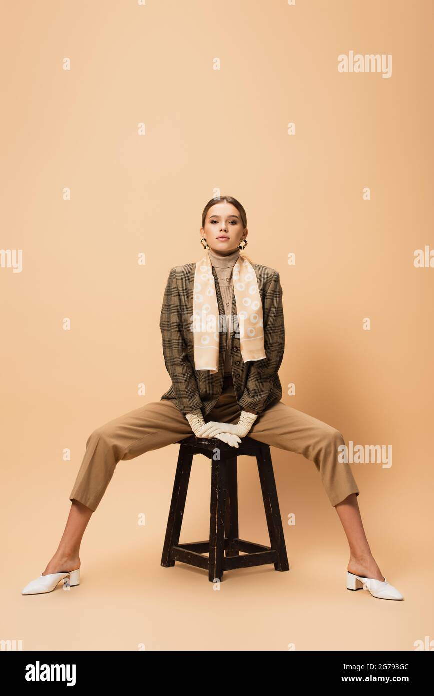 front view of stylish woman in brown blazer and pants posing on wooden ...