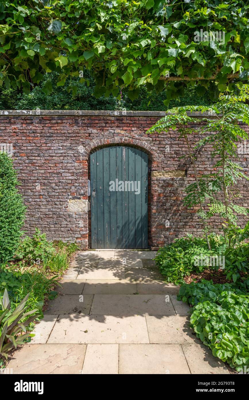 A green walled garden door in a red brick wall with a slabed footpath Stock Photo