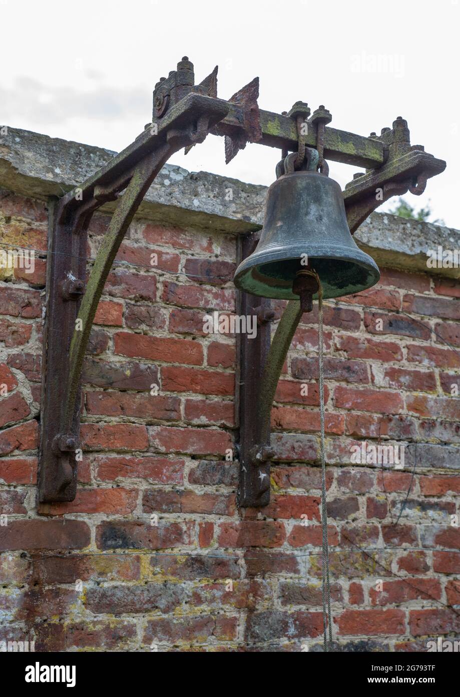 A large bell mounted on a brick wall with metal work and pull string
