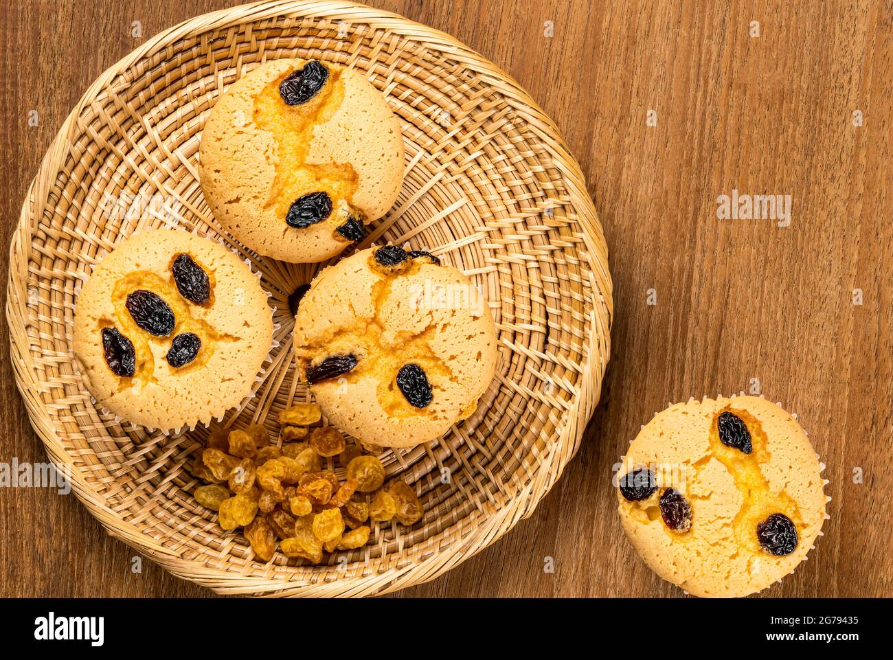 Top view of raisin sponge cupcake with pile of dried sweet raisin in bamboo tray and single raisin sponge cupcake on wooden table. Stock Photo