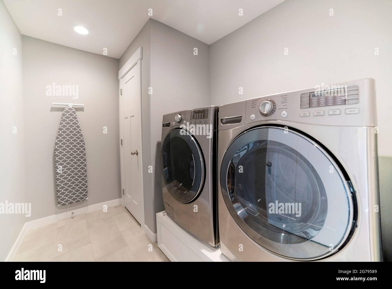 Light gray laundry room with tiles, washer, dryer and storage room
