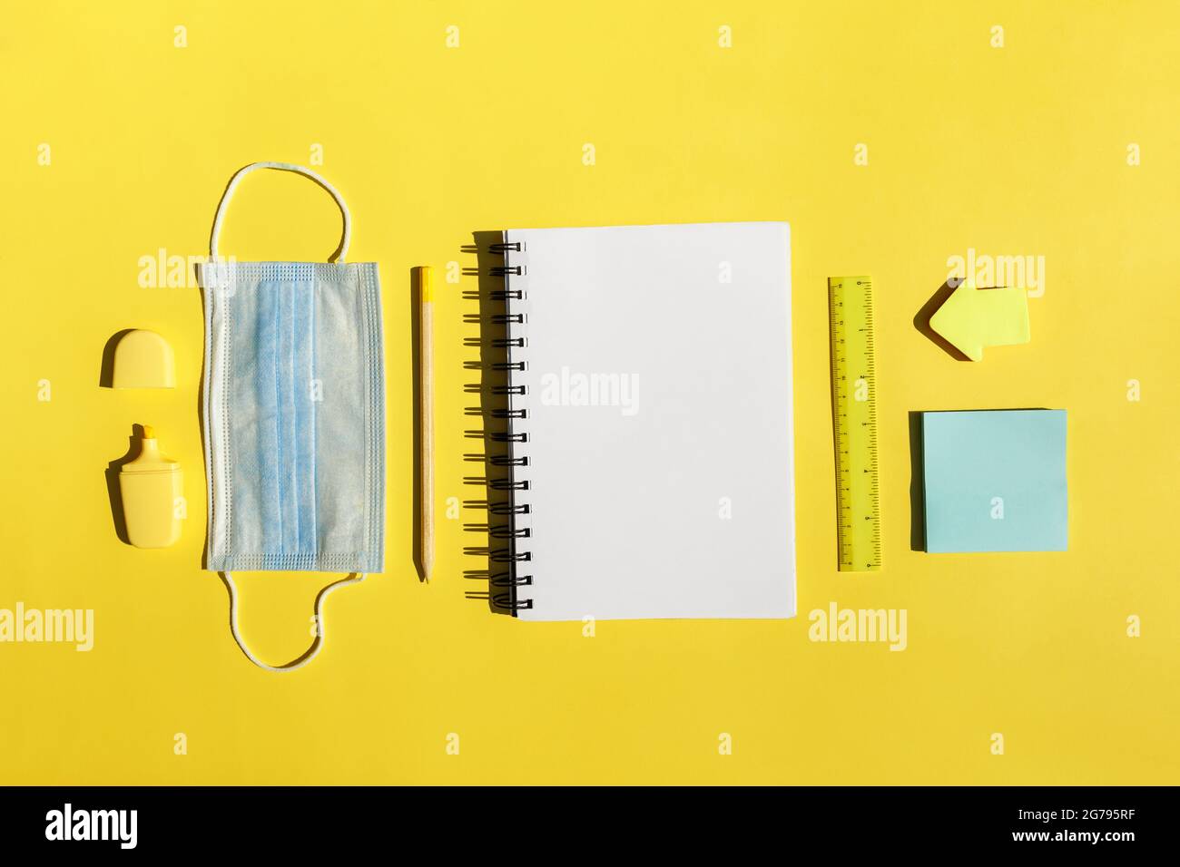 School stationery supplies, notebook, medical mask on yellow background social distancing, school reopening after covid-19 pandemic. New normal concept.Top view copy space,blackboard. Stock Photo