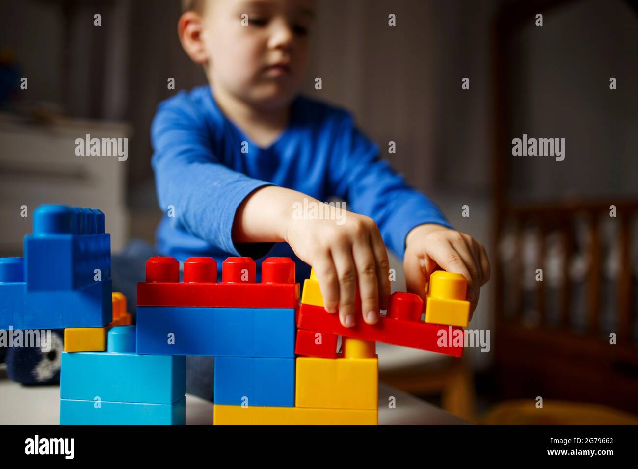 Imagination development technique. Selective focus on creative constructions built by a child sitting at a table and concentrating on a new plastic masterpiece in the background. High quality photo Stock Photo