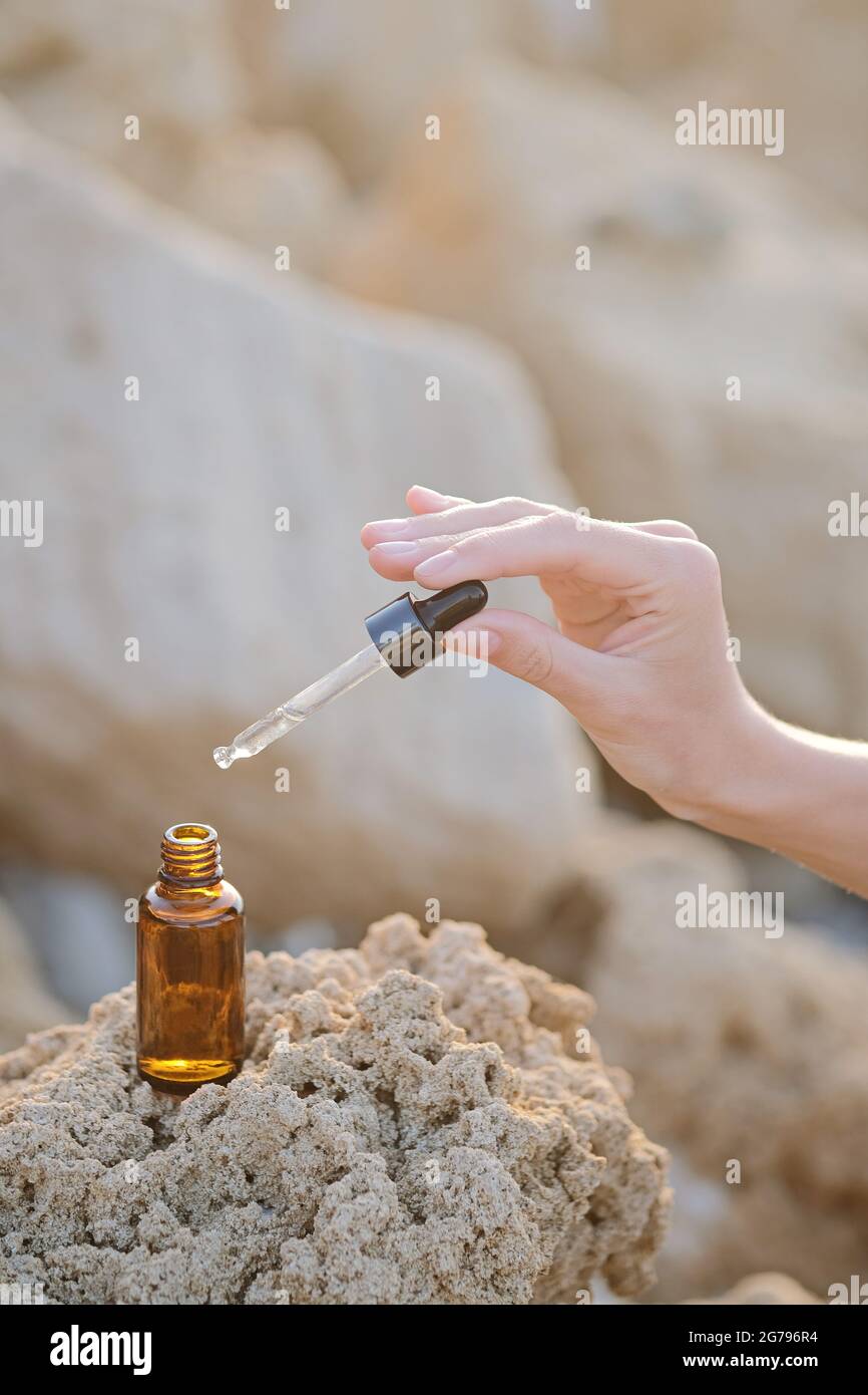 Cosmetic jar with cream, serum or organic essential oil for the face and body, against the background of a natural stones in sunset light. beauty salon and natural cosmetics. Hand hold dropper. Stock Photo