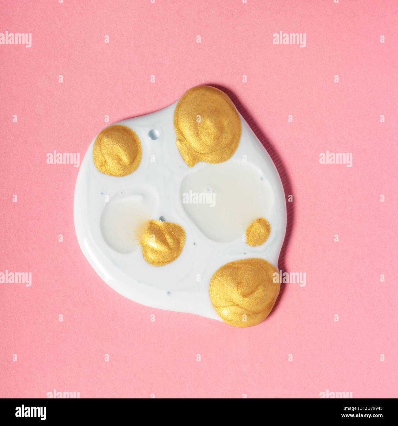 White skincare product dollop with golden drops on pink. Cosmetic skin emulsion formula textured glowing swatch, active ingredients concept Stock Photo