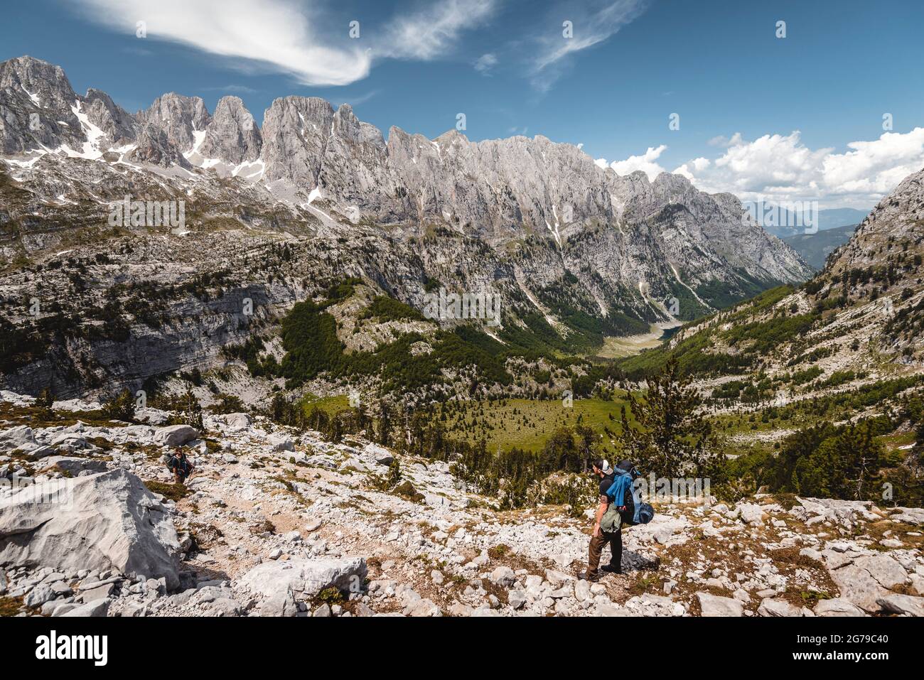 In bright sunshine, a single hiker looks out over the landscape of the Prokletije National Park to a huge mountain range, Albania Stock Photo
