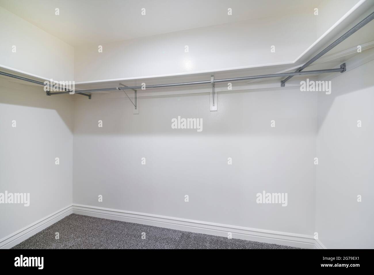 Empty walk in closet with metal hanging rods and wooden shelves Stock