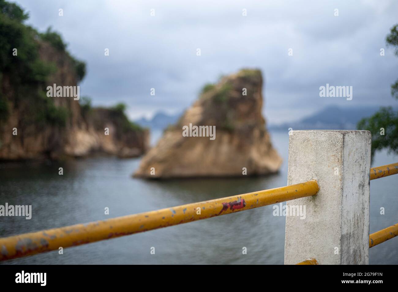 The view from Ponte da Boa Viagem, Niterói, State of Rio de Janeiro, Brazil. Green Ilha da boa Viagem private island in bay connected to main land via narrow bridge and yellow sand under blue cloudscape. Mountains in distance. Stock Photo