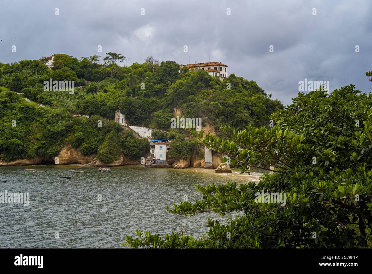 The view from Ponte da Boa Viagem, Niterói, State of Rio de Janeiro, Brazil. Green Ilha da boa Viagem private island in bay connected to main land via narrow bridge and yellow sand under blue cloudscape. Mountains in distance. Stock Photo