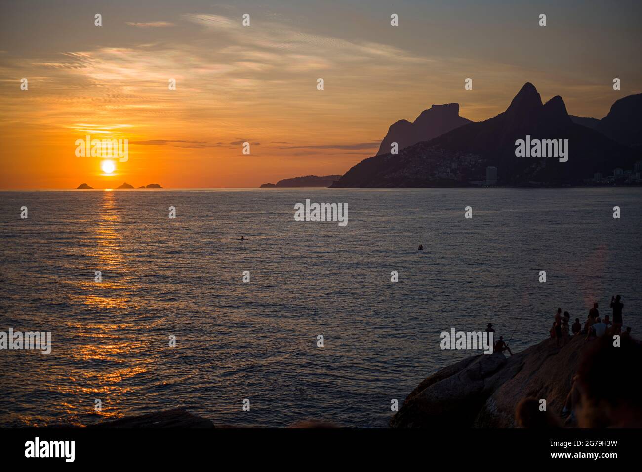 A magical place: People applaud when the sun sets at Arpoador rock with view of Ipanema beach and the Mountains of Morro Dois Irmaos and Leblon in the back. Camera: Leica M10 Stock Photo