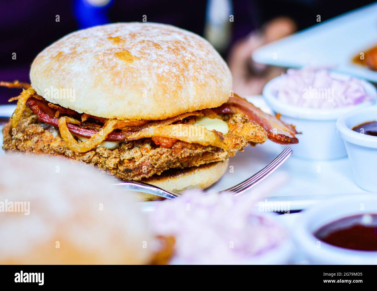 Burger with Meat, Bacon, Fried Onions & Coleslaw on Restaurant Table Stock Photo