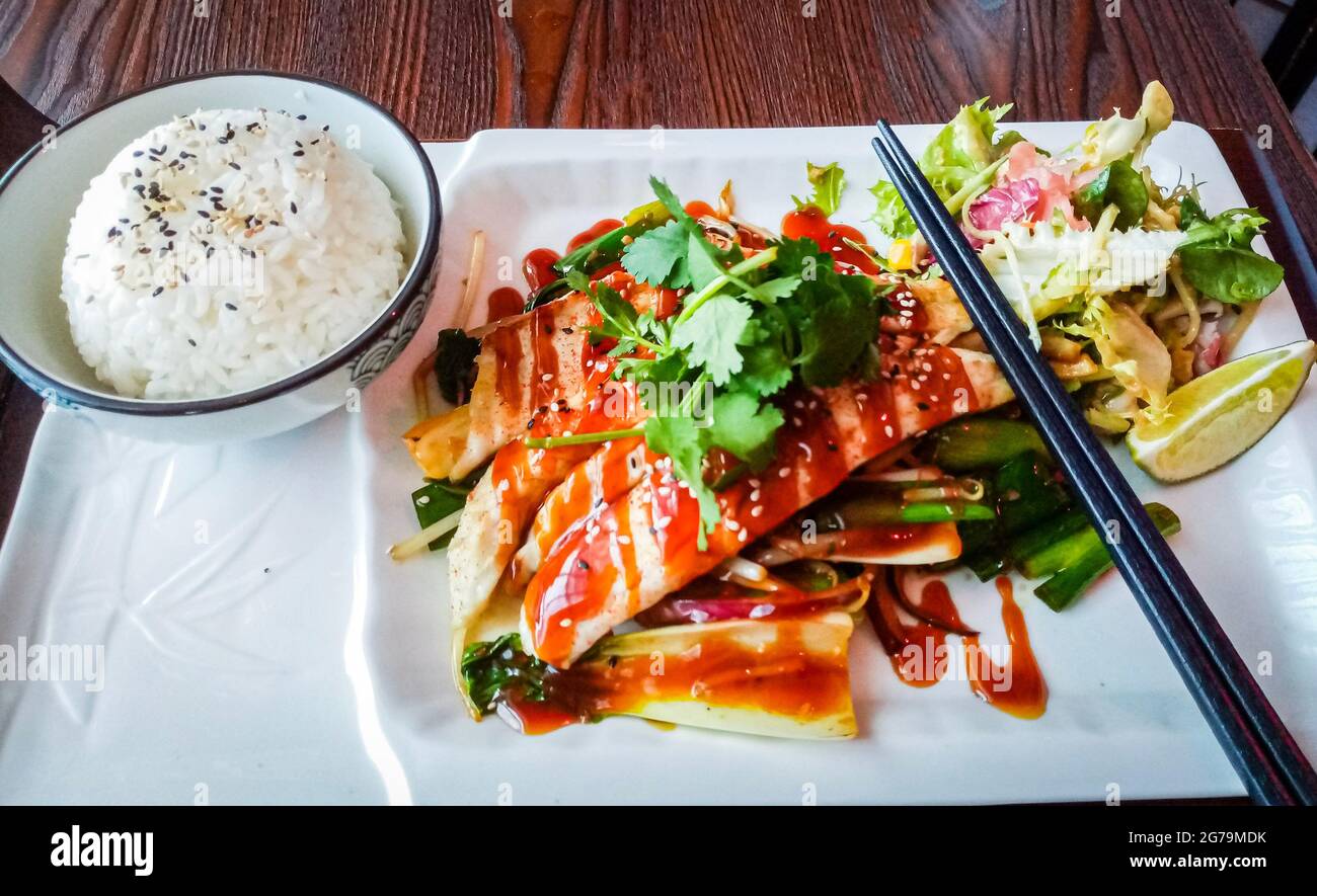 Japanese Suzuki Amiyaki Gohan, grilled sea bass with coriander, mix vegetables and steamed rice placed on restaurant table. Stock Photo