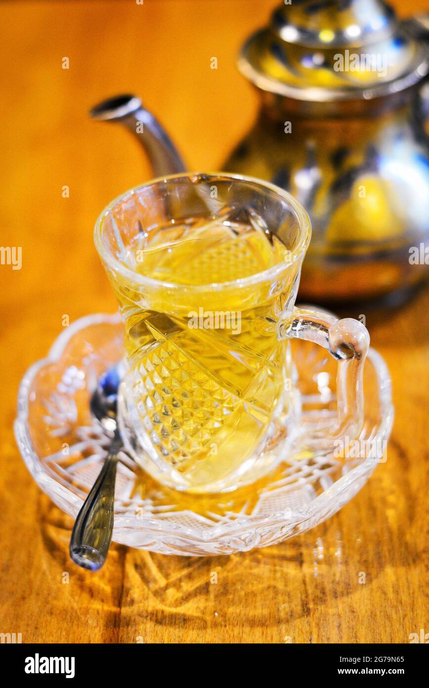 Lebanese tea in a glass cup placed on table with tea pot blurred at background Stock Photo