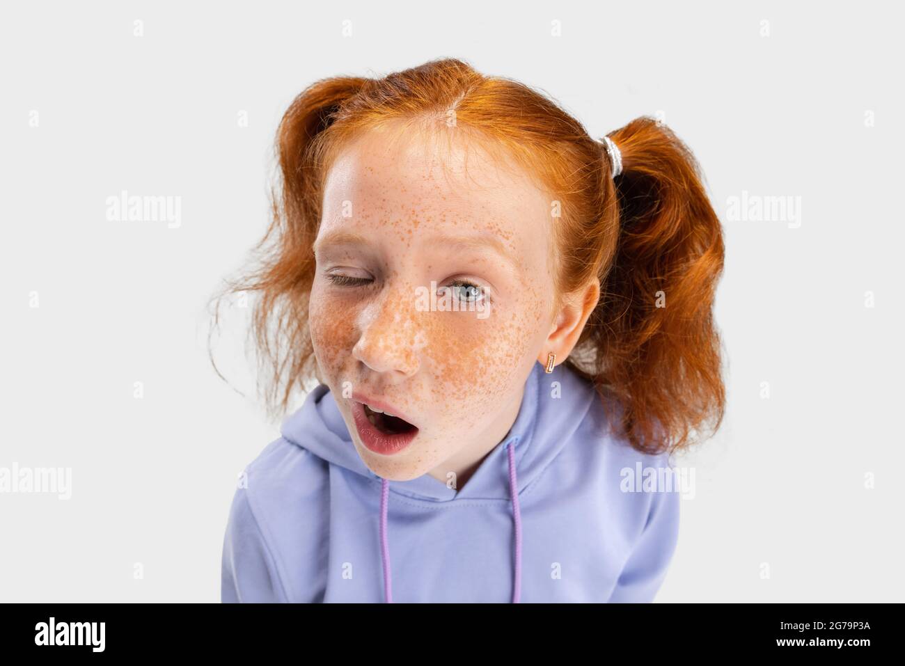 Close-up funny girl with freckled face and red hair looking at camera isolated on white studio background. Happy childhood concept. Sunny child Stock Photo