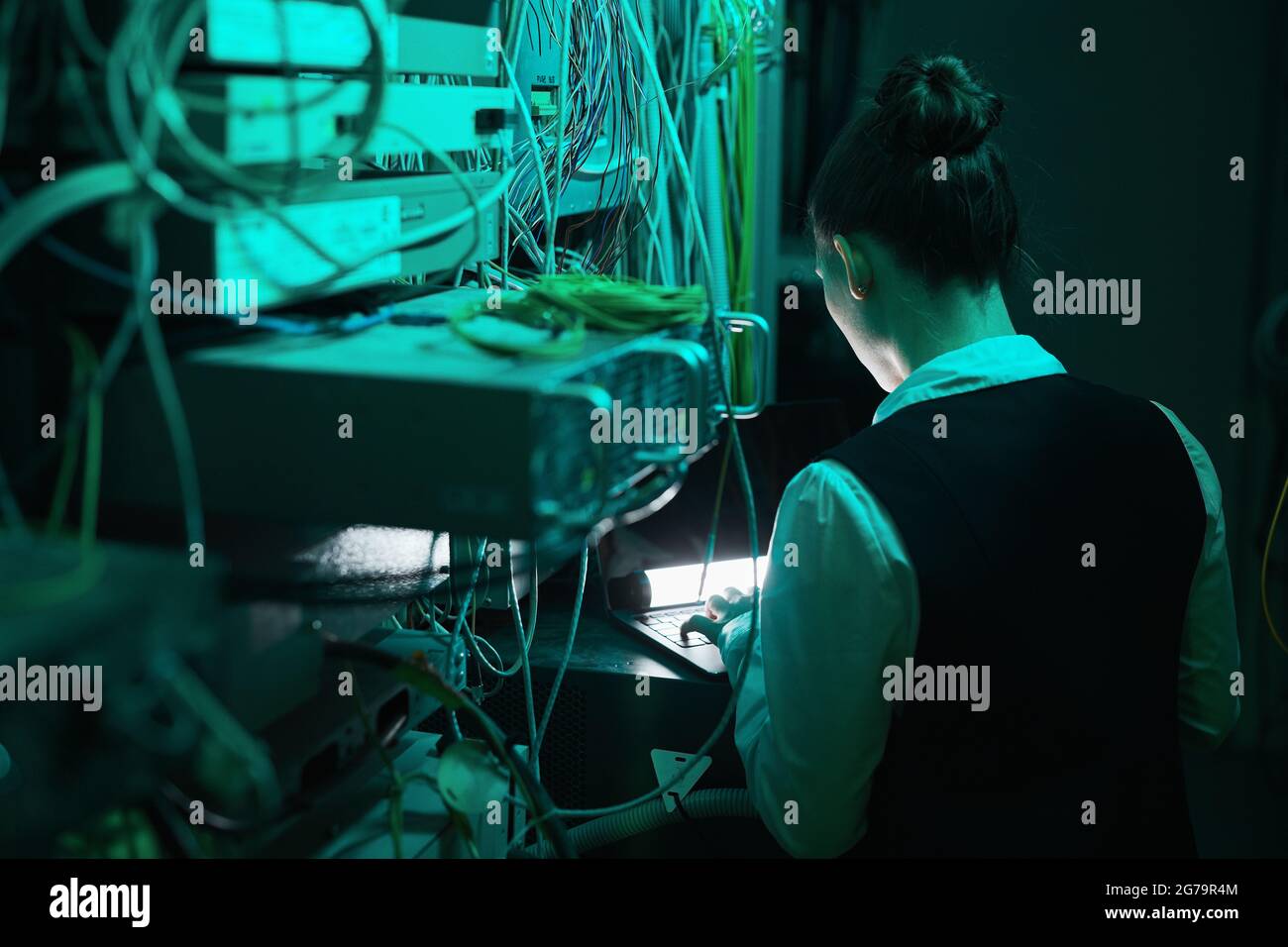 Back view of female network engineer inspecting servers while working with supercomputer in data center, copy space Stock Photo