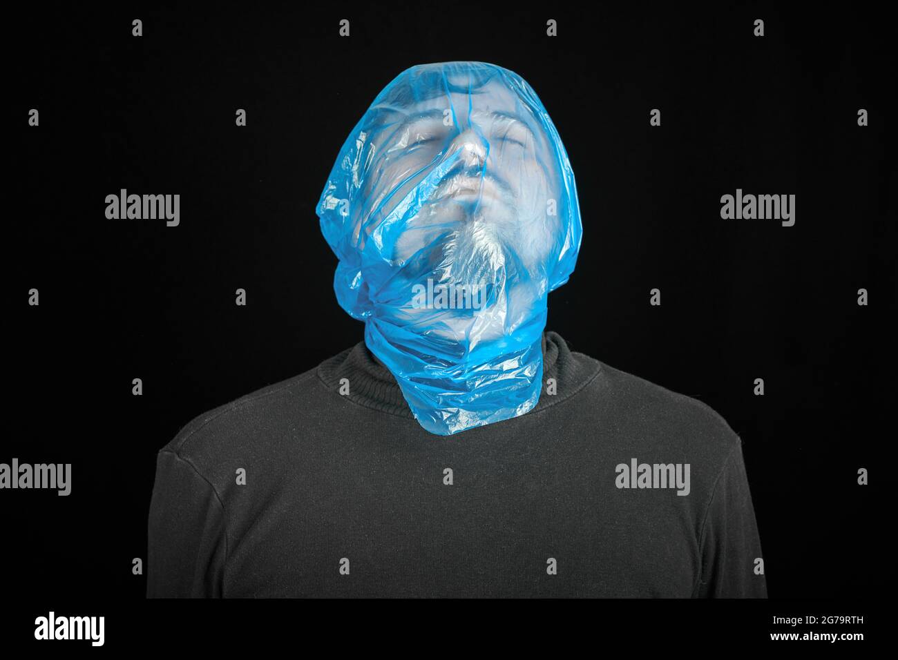 Suicide bag on man head. Exit bag for suicide. Self-asphyxiation concept. Garbage bag on head. Shortness of breath, lack of air. Black background. Stock Photo