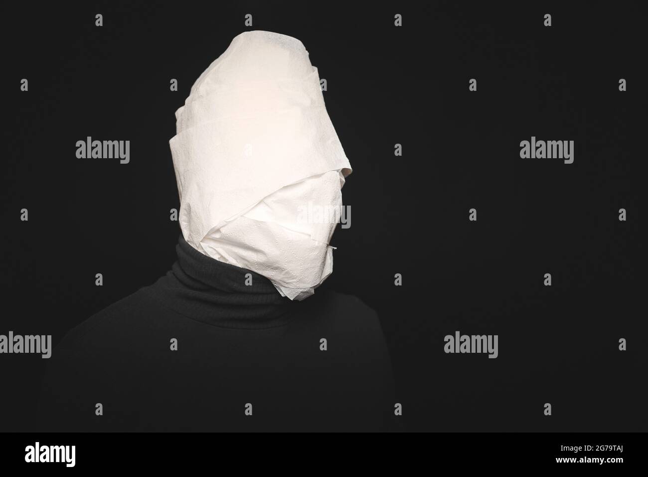 Head wrapped in toilet paper. Funny man, black background. Mummy, stupid dummy, mental health concept. Stock Photo