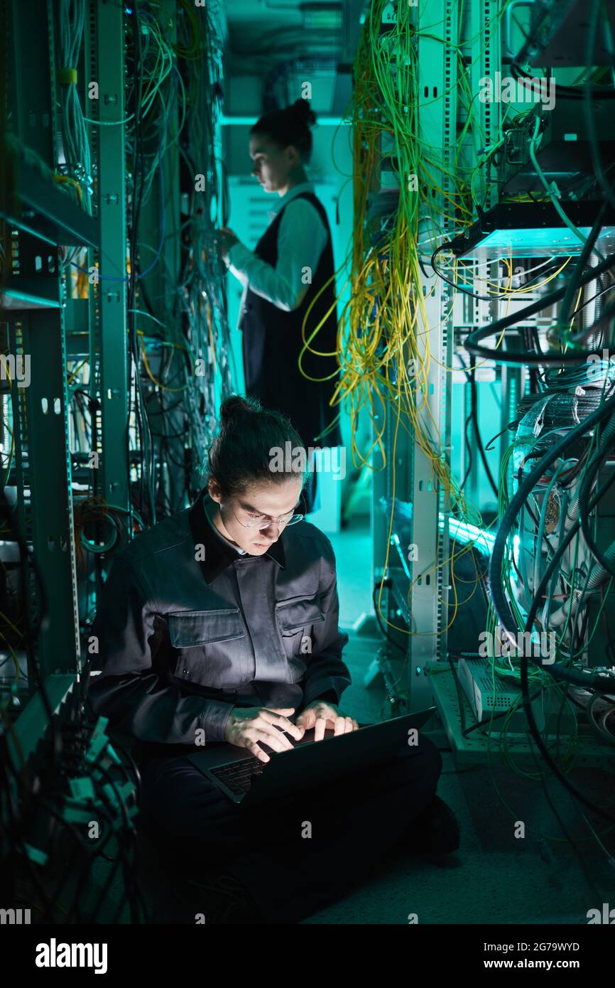 Vertical portrait of young technician setting up computer network in server room Stock Photo