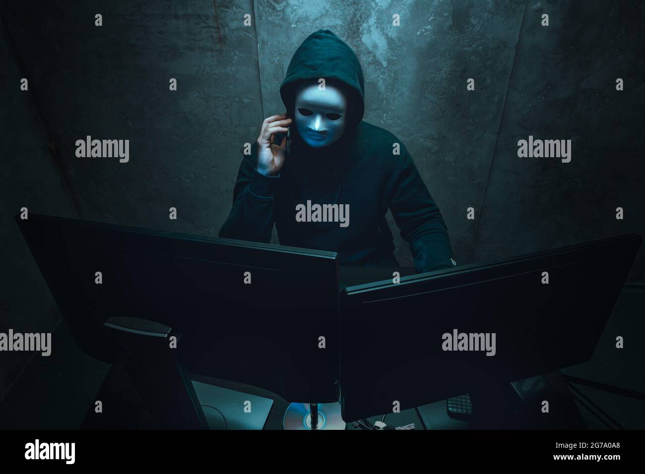 Anonymous hacker wearing face mask working on computer in dark room ...