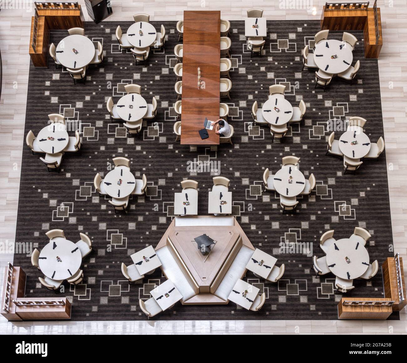 Aerial view above a hotel restaurant or cafe tables wtih a single man working on laptop in empty room Stock Photo