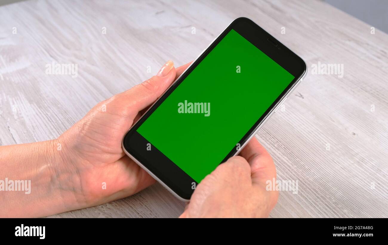 Hands of a middle-aged woman senior uses a smartphone iPhone with a chroma key screen, copy space. Online shopping concept, use of mobile applications Stock Photo