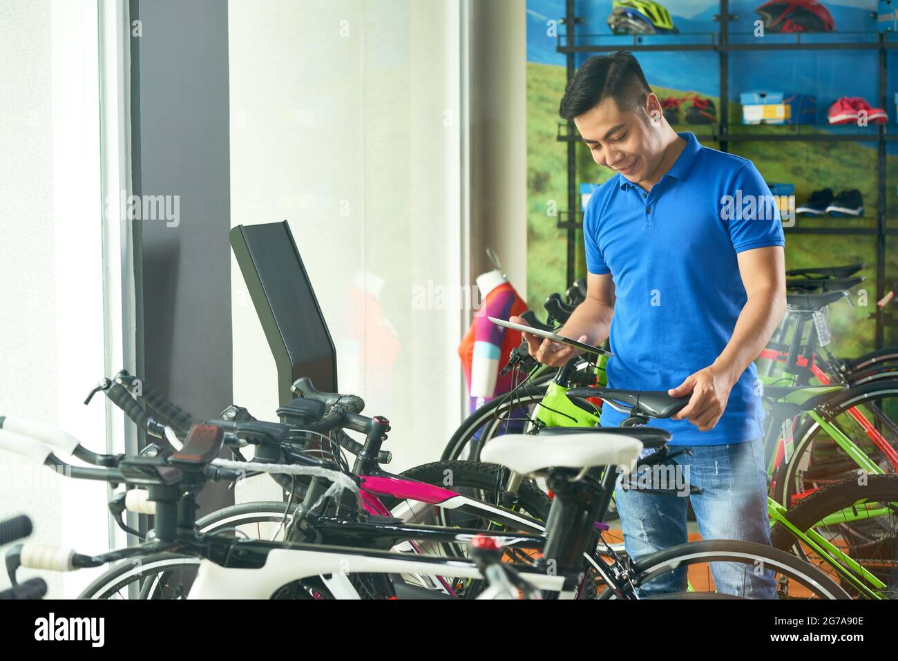 Cheeful salesman of bicycle store reading and memorizing characteristics of every vehicle Stock Photo