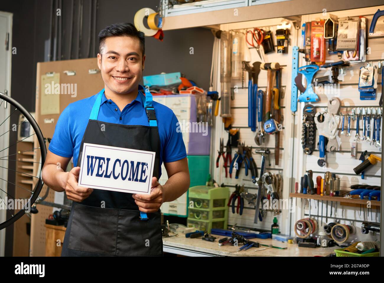 Portrait of smiling mechanic opening workshop and welcoming customers with broken bicycles Stock Photo