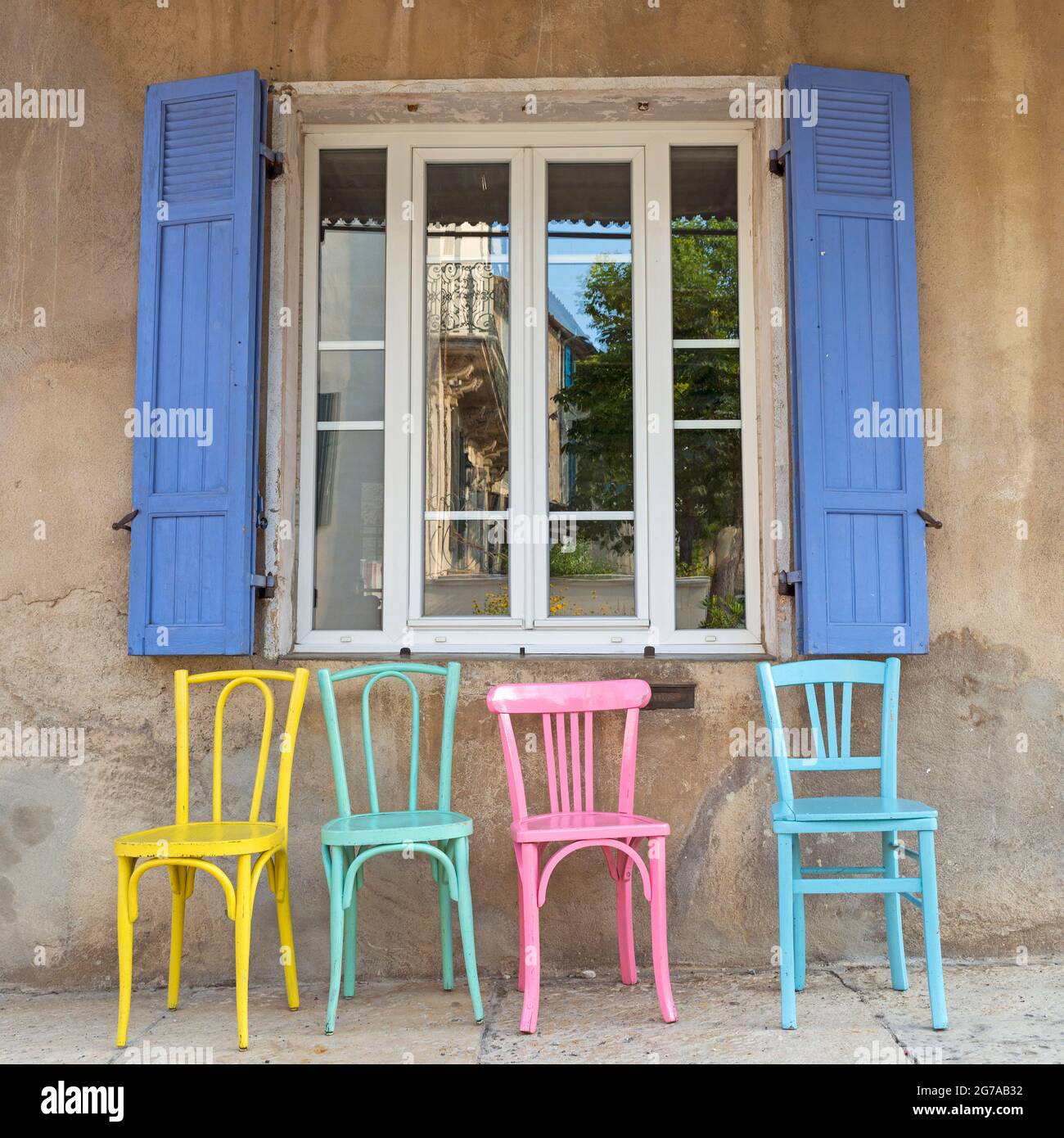 colorful wooden chairs stand in front of a window on the street, Provence, France Stock Photo