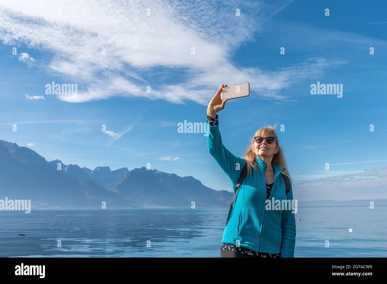 Happy woman enjoying day in the mountains and taking a selfie with her phone. Stock Photo