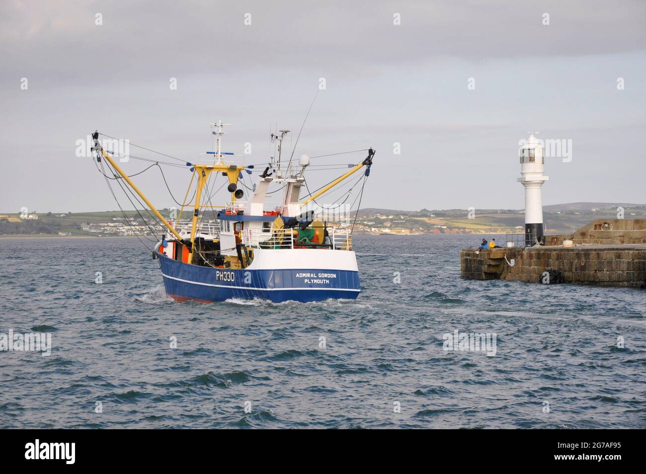 A Plymouth registered Trawler passes out of Penzance harbour into Mounts Bay past the light on end of the quay. Penzance. Cornwall. UK Stock Photo