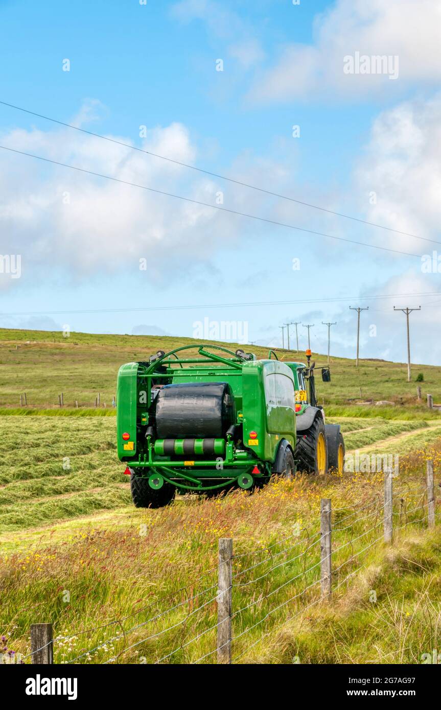 John Deere tractor towing McHale Fusion 3 integrated baler wrapper making sileage in Shetland. About to eject wrapped bale. Stock Photo