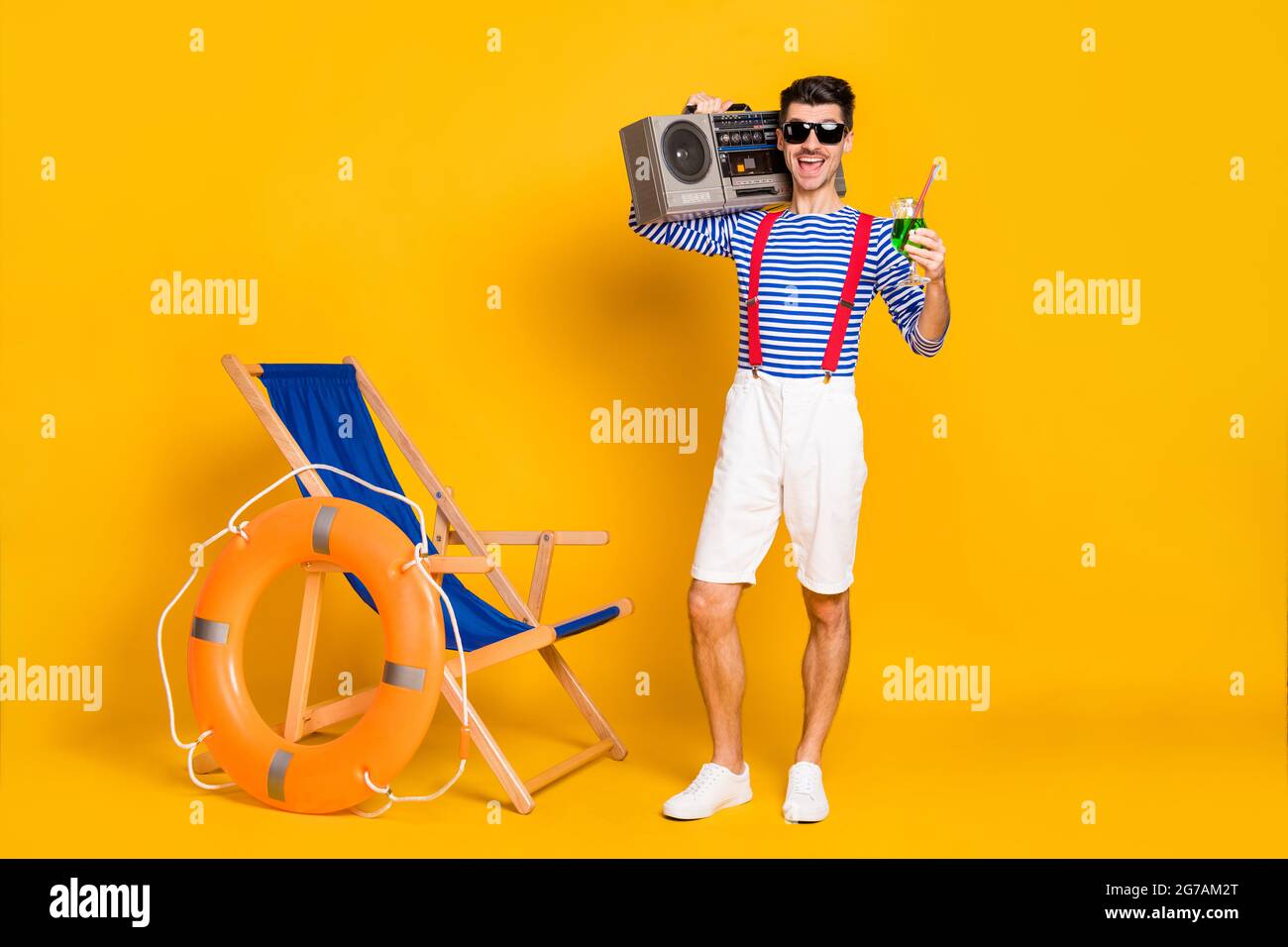 Full size photo of handsome brunette man hold boombox cocktail beach wear sailor outfit isolated on yellow color background Stock Photo