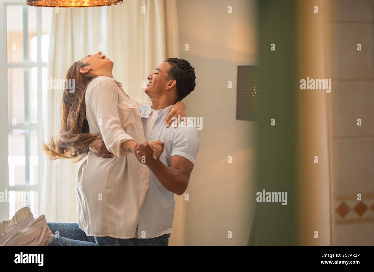 Happy mixed race ethnicity husband and wife feel excited dancing swaying standing at home, smiling overjoyed couple have fun celebrating anniversary swirling and dancing together in love Stock Photo