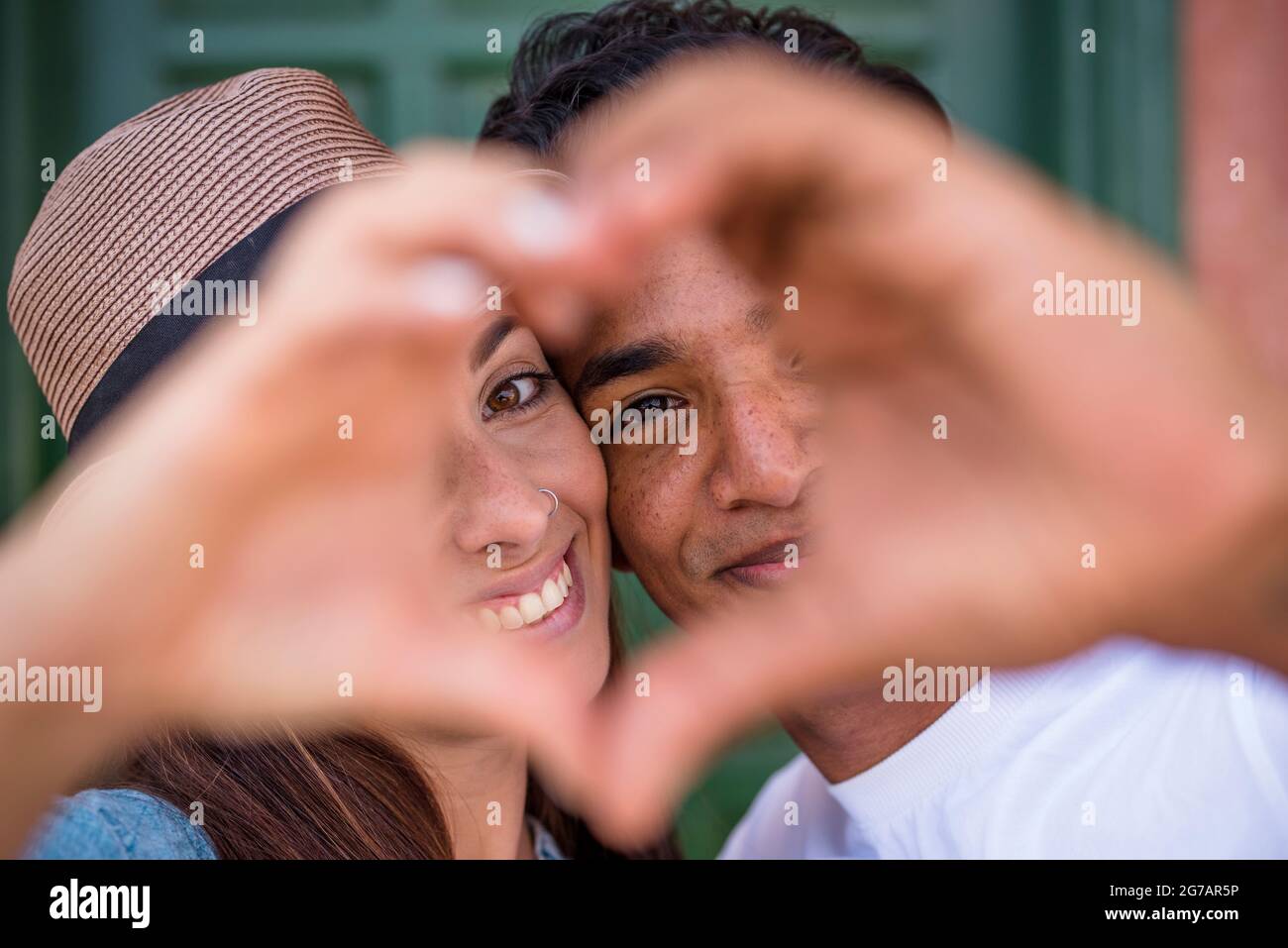Mixed race couple do hearth sign with hands, looking to camera - love and relationship concept with young man and woman - boyfriend girlfriend together - friendship millennial boy and girl Stock Photo