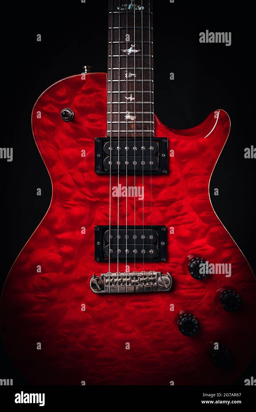 Closeup of a red shiny guitar body showing pickups, strings and