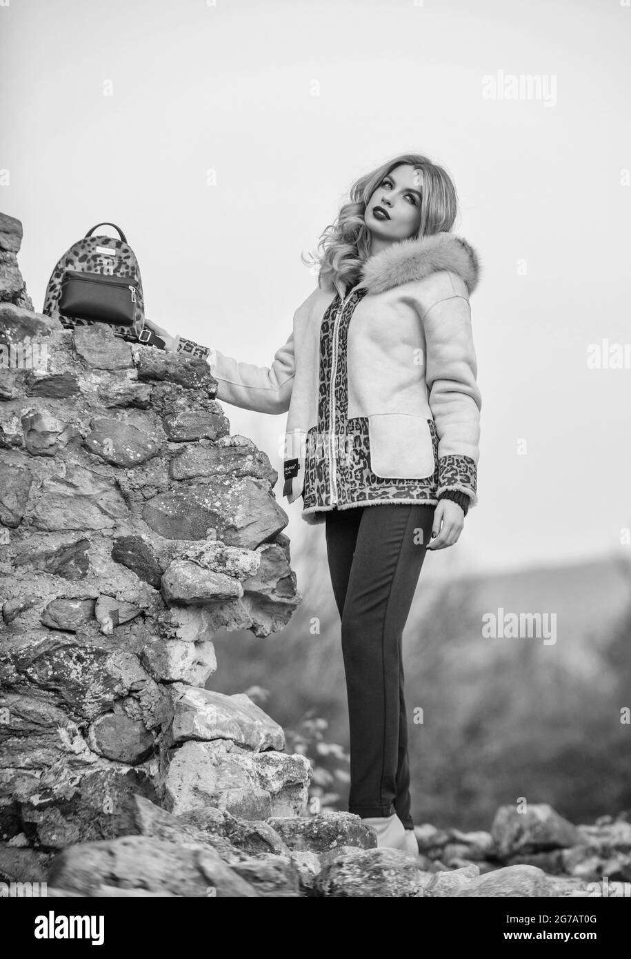 Wardrobe for cold weather. Girl stand near stone ruins. Fancy chic coat. Natural wool sheepskin coat. Fur on hood. Hit of season. Stay warm and Stock Photo