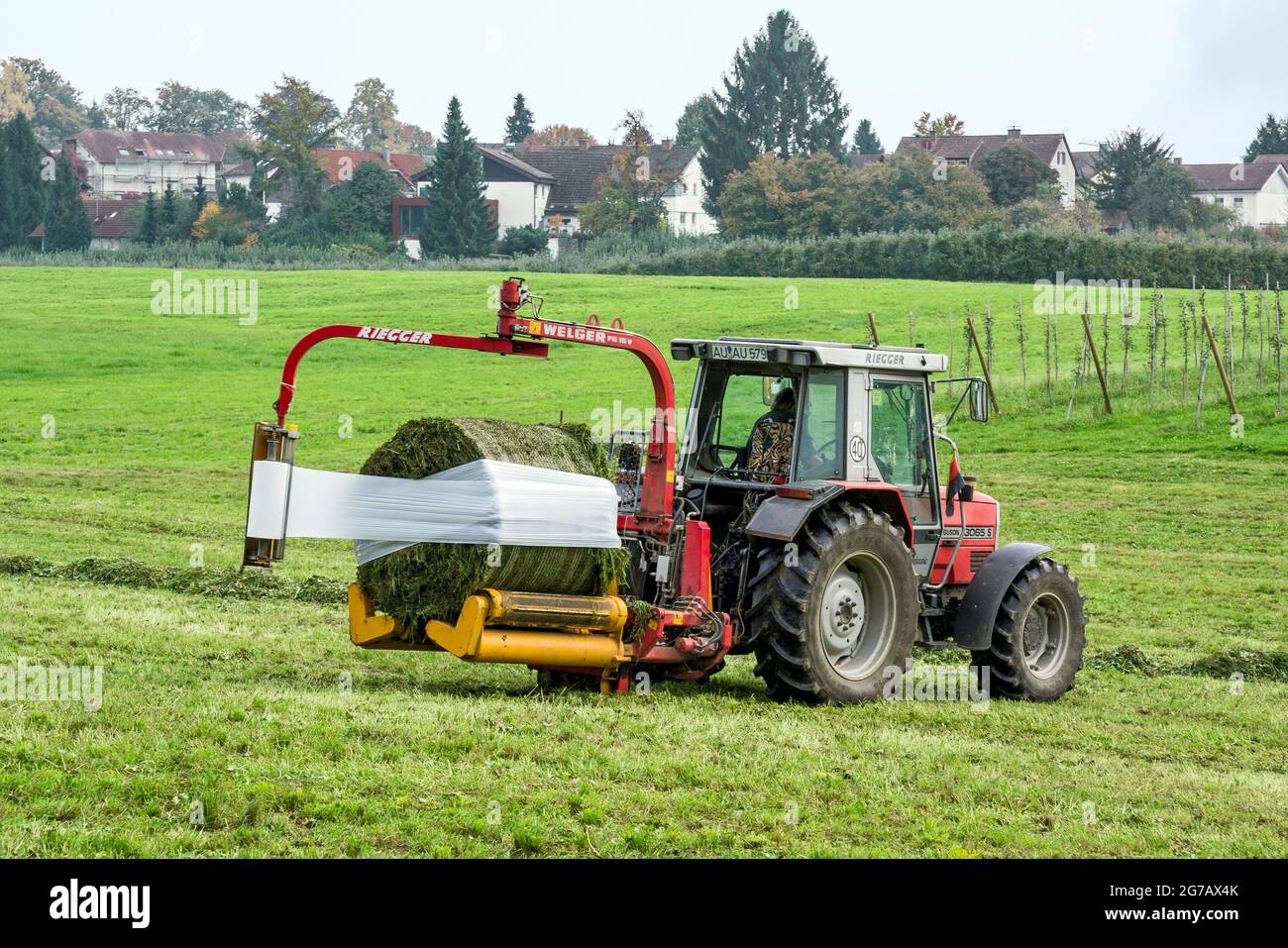 Germany, Baden-Wuerttemberg, tractor with round bale wrapper at the forage harvest Stock Photo
