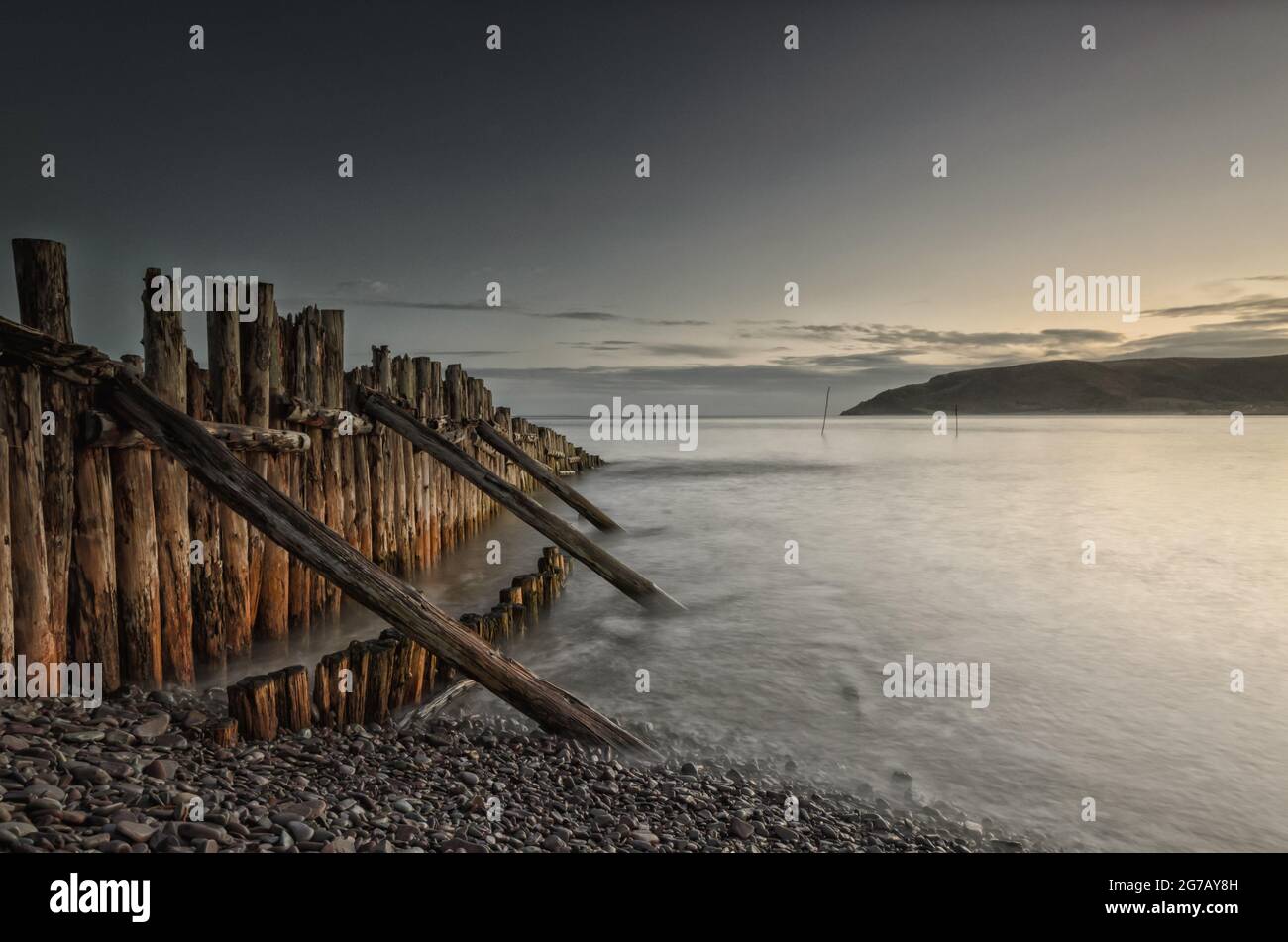 Old wooden groynes extending out from the shingle beach into the Bristol channel catching the pre-dawn light. A long exposure smooths out the water. Stock Photo