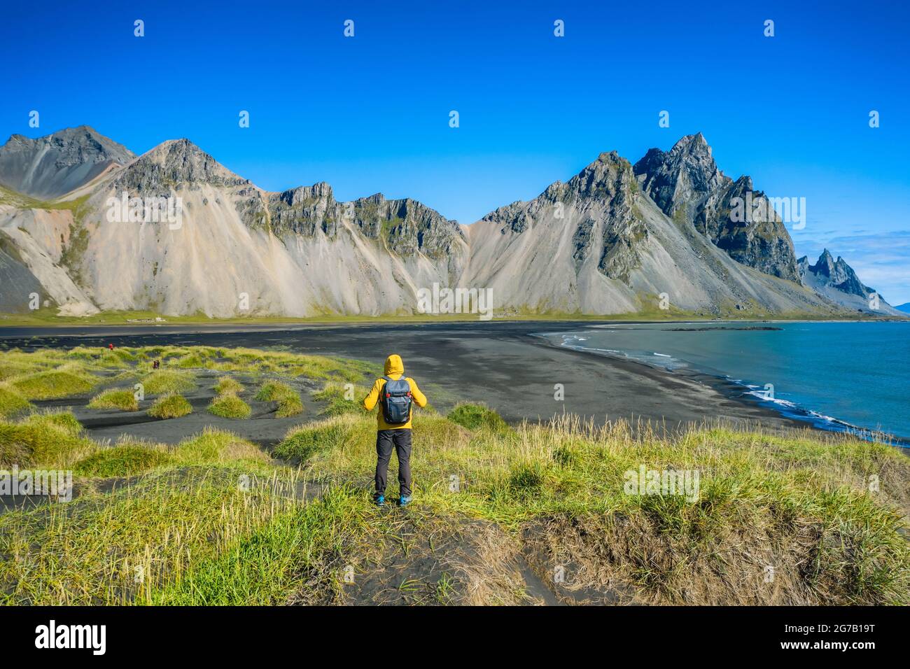 Man hiker with backpack at black sand dunes on the Stokksnes headland on southeastern Icelandic coast with Vestrahorn. Colorful summer morning Iceland, Europe. Stock Photo
