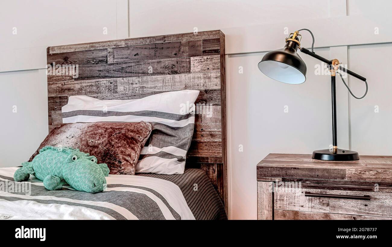 Pano Lamp on side table beside bed with wooden headboard against panelled wall Stock Photo Alamy