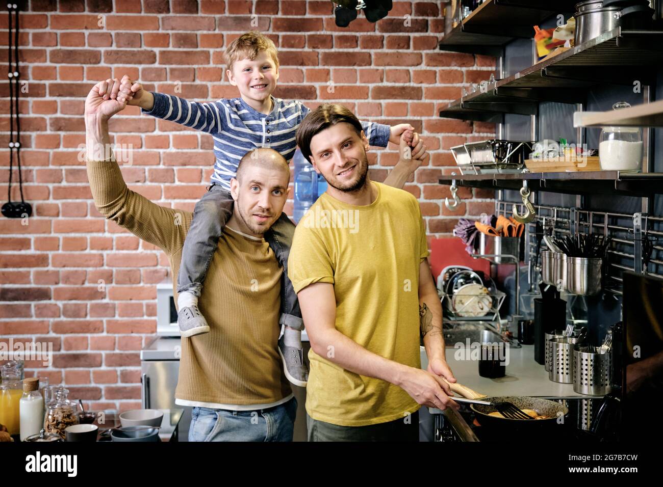 Portrait of happy gay family of two fathers and little boy standing in kitchen and cooking breakfast Stock Photo