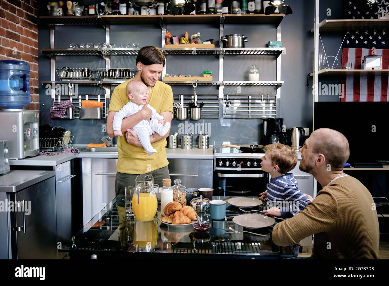 Happy smiling gay man introducing newborn baby to his older son at family breakfast Stock Photo