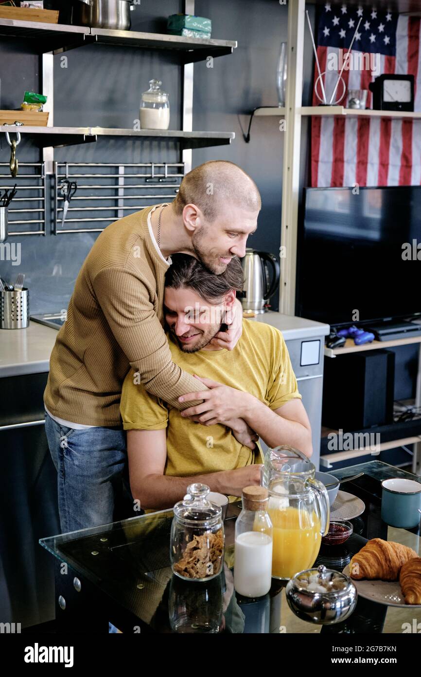 Happy young LGBT couple in love hugging and cuddling at home after eating tasty breakfast Stock Photo
