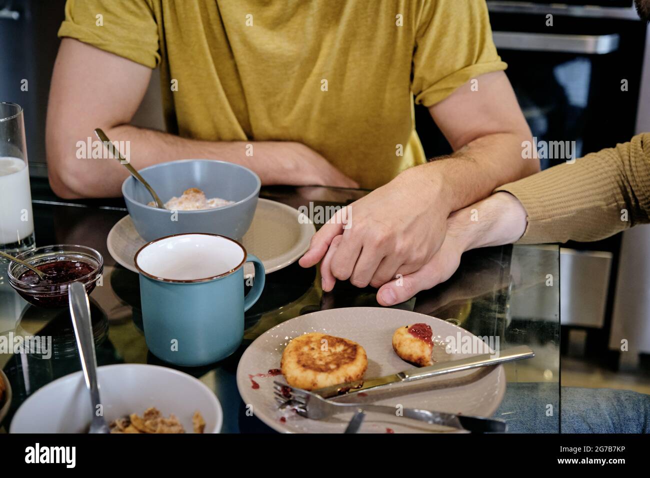 Two guys holding hands when eating breakfast together at home Stock Photo